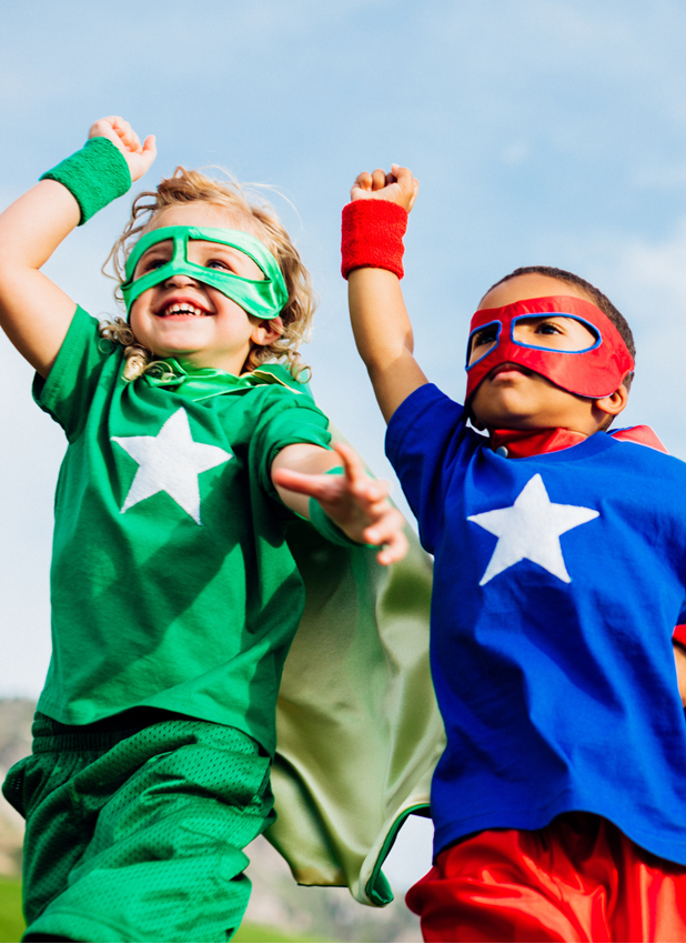 two boys dressed as superheros with arms in the air